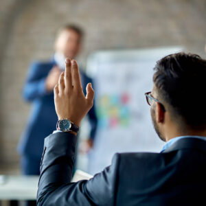Person in suit raising their hand to ask a question during presentation