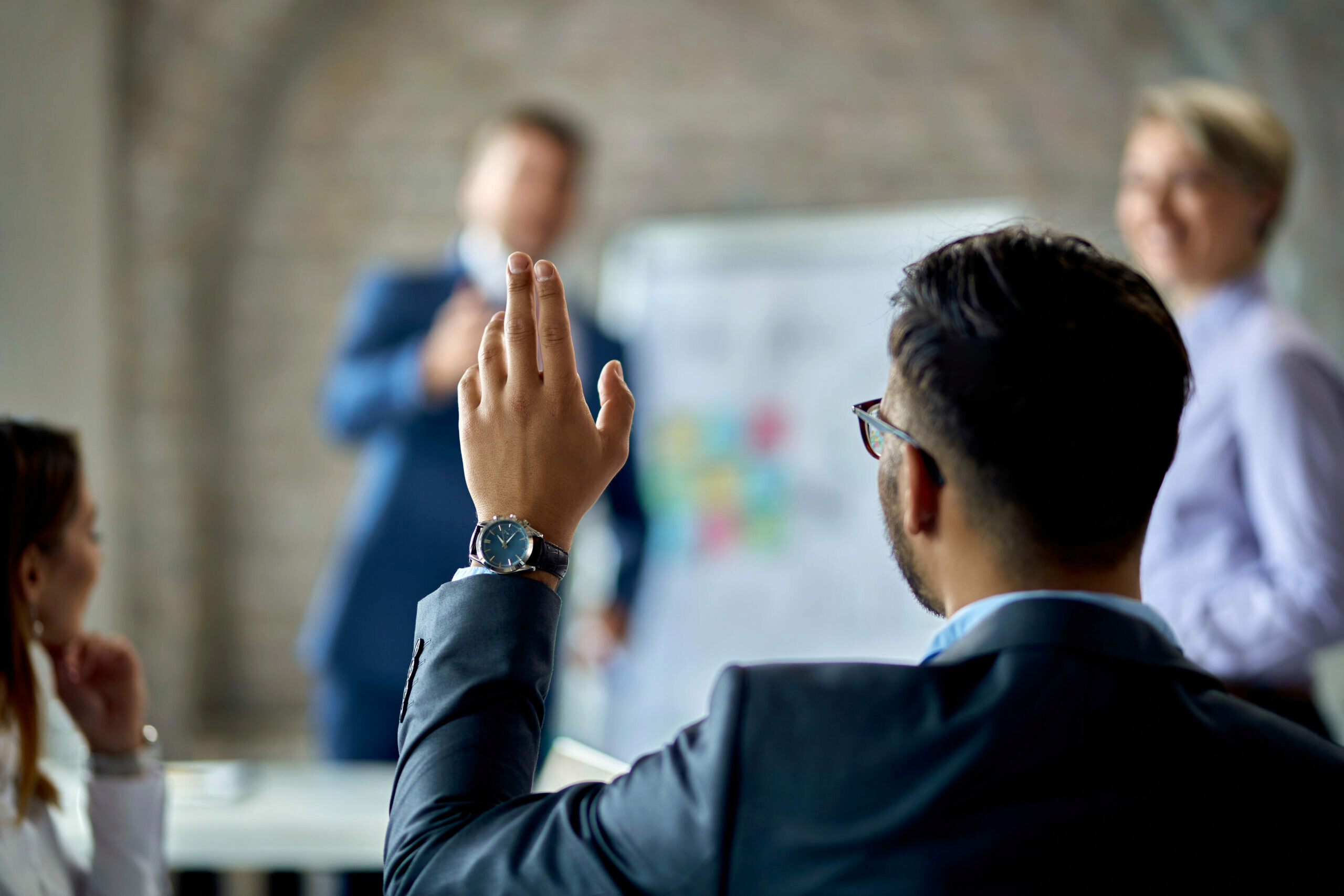 Person in suit raising their hand to ask a question during presentation