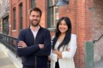 Cofounders of Twentyeight Health posed smiling with their arms crossed on a street in front of red brick buildings.