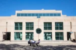 Image of the Annenberg School of Communication on a sunny day with people sitting at a table and chatting out front.