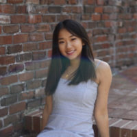 Izzy Zhang smiling in a blue and white striped dress posed sitting on red brick steps in front of a brick wall.