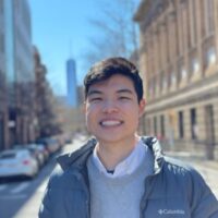Jeffrey Chen smiling in a grey puffer layered over a light grey sweater and white button up on a city street.