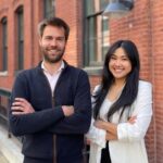 Bruno Van Tuykom and Amy Fan, cofounders of Twentyeight Health, smiling and posing on a city street in front of a red brick building