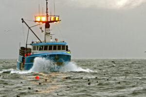 Stock image of a blue fishing boat with its lights on during a cloudy day in the ocean