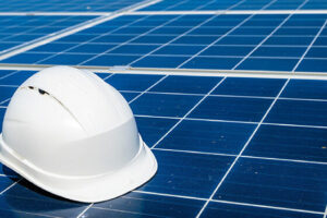A white hard hat sits atop a blue grid of solar panels receding into the distance.