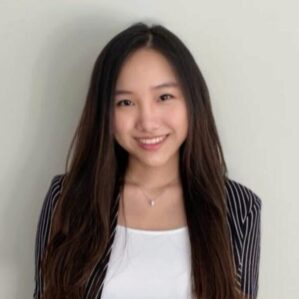 Sapphira Ching smiling in a black and white pin stripe blazer and a white shirt against a white wall