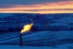 A natural gas flare on an oil well pad burns as sun sets in front of a natural landscape.