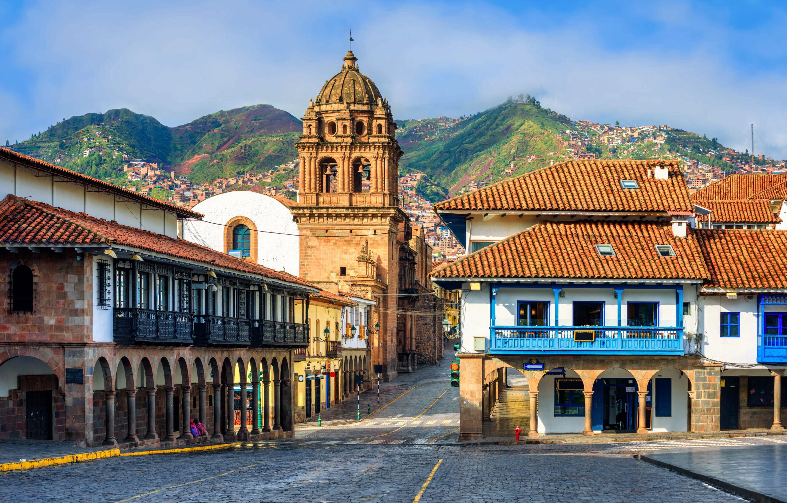 Decorative image of the Plaza Mayor And Basilica Menor Church in the foreground and big green mountains in the background under a bright blue sky
