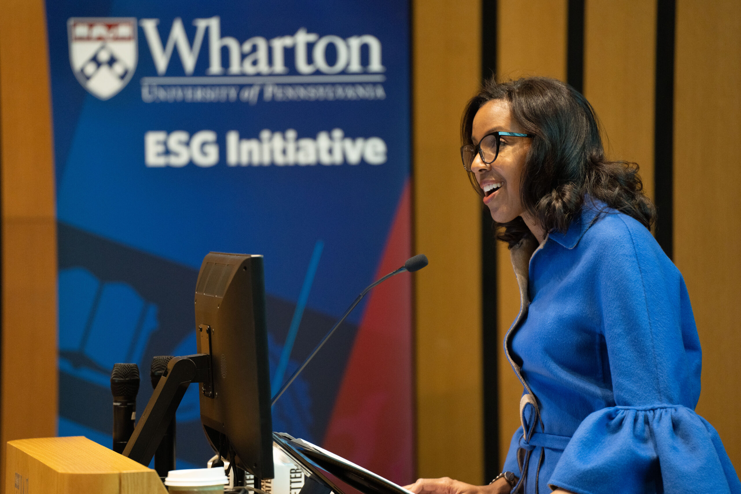 Dean James in a blue blouse smiling and speaking at a podium with a banner in the background that says "Wharton ESG Initiative"