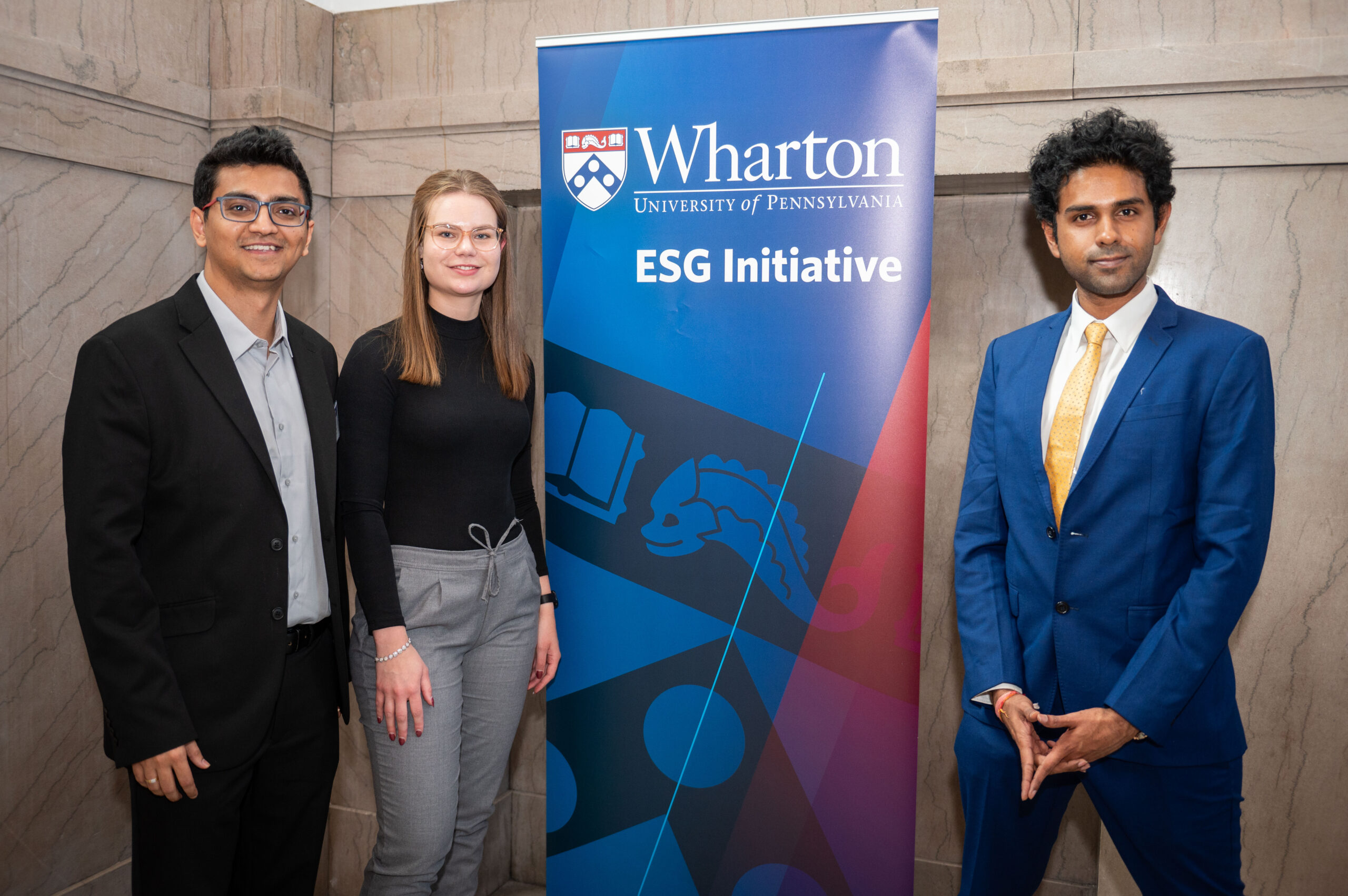 Three members of the Fletcher School at Tufts University team pose in professional attire next to a banner that reads "Wharton ESG Initiative"