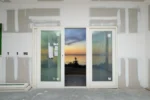 A wall with paint and door facing into a sunset with signs posted to the open window/doors.