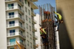 Construction workers climb on construction site in front of a tall apartment building