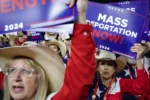 A crowd of people dressed in red, white, and blue and wearing cowboy hats wave signs that read "Mass Deportation Now!"