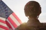 The back of the head of a soldier with an American flag in the background.